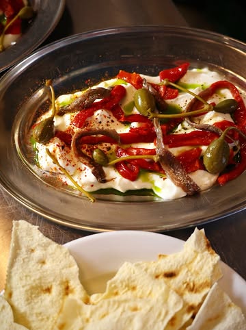 Labneh maison, câpres, poivrons confits, anchois et pain sarde, à grignoter le soir.