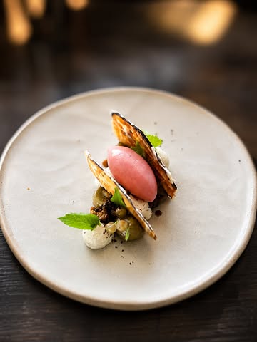 Et si l’aubergine devenait un dessert ?

Cueillie à pleine maturité chez notre partenaire @biok.be , elle est ici travaillée sous plusieurs formes : en caviar sucré au caramel et à l’agastache, mais aussi en fins croquants pour apporter de la texture.

Ses notes végétales sont adoucies par une ganache au chocolat blanc délicatement relevée de poivres. L’ensemble est réveillé par un sorbet à la groseille de notre jardin, rehaussé de poivre de Sichuan frais, qui pousse naturellement dans notre potager.

Une assiette surprenante, fraîche et équilibrée, où le légume trouve naturellement sa place dans l’univers du dessert.